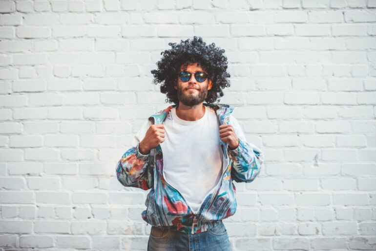 Stylish young man in a retro jacket. Fashion trends of 90s. Handsome hipster guy with beard with curly hair.